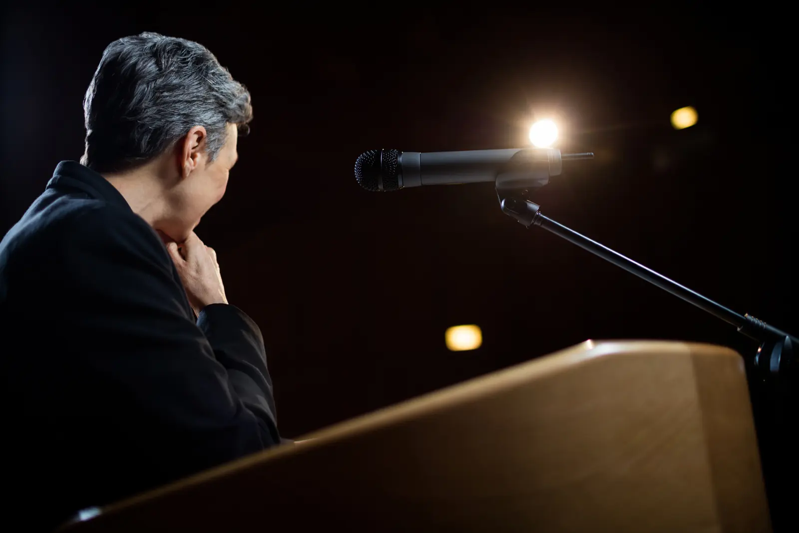 A public speaker at a lectern under warm stage lighting